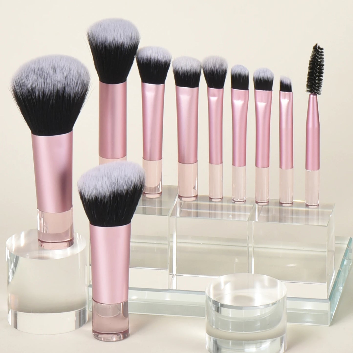 10 piece light pink travel makeup brush on a acrylic display. Made with synthetic nylon fibers. Great for beginner makeup artists. Comes with blush brush, foundation brush, eyeshadow brush, eyeshadow smudger, eyeshadow detailer brush, angled eyebrow brush, lipstick brush and an eyebrow spoolie.
